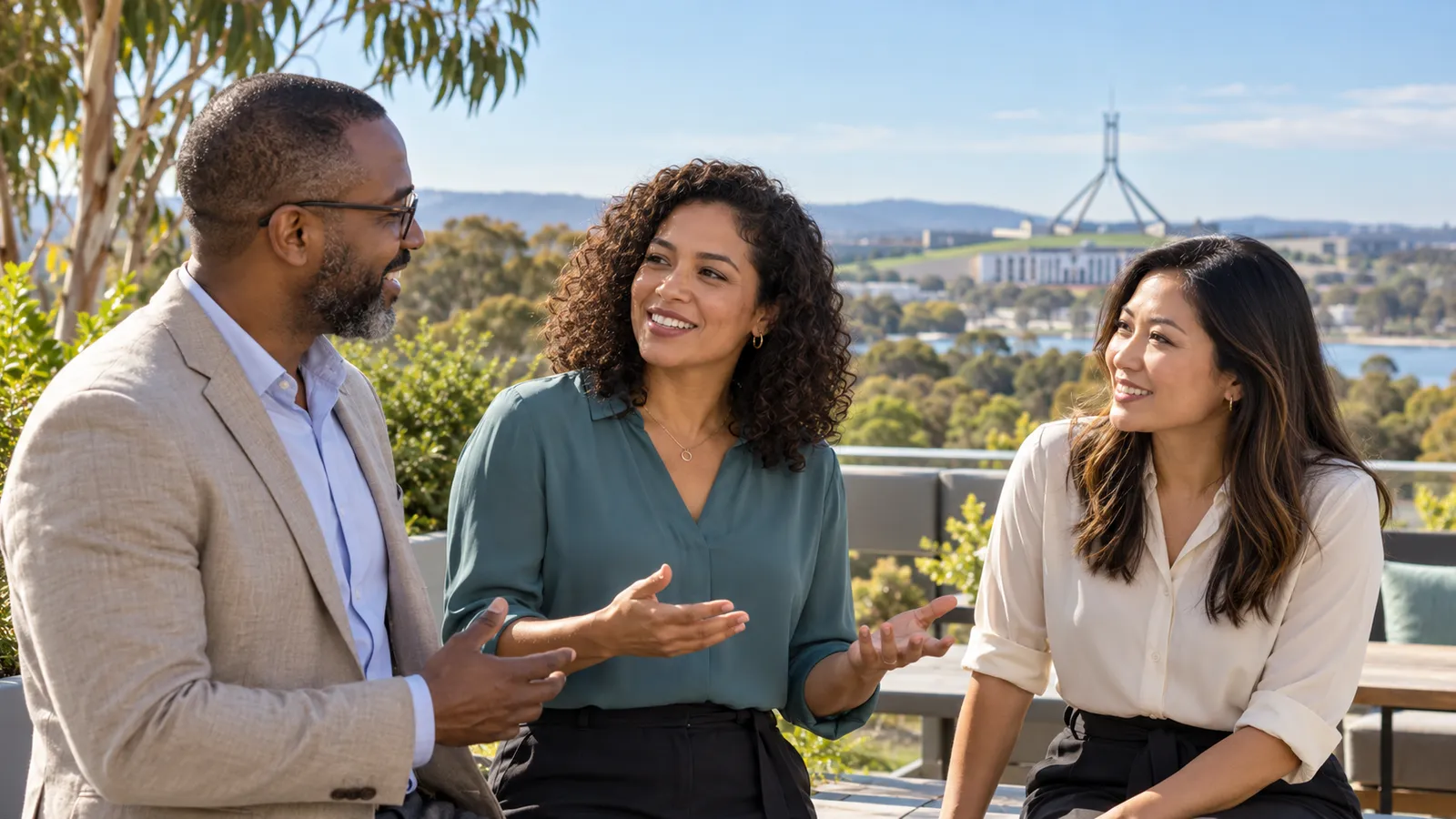 Três profissionais brasileiros conversam em um terraço ensolarado, com o Parlamento australiano ao fundo, em Canberra.
